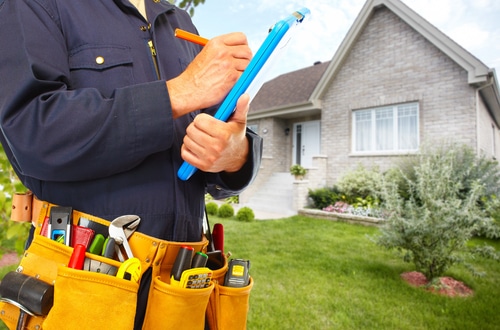 The mid-section of a man outside of a house writing a proposal for plumbing work.