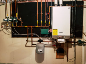A tankless water heater along the wall with several pipes running multiple different directions.