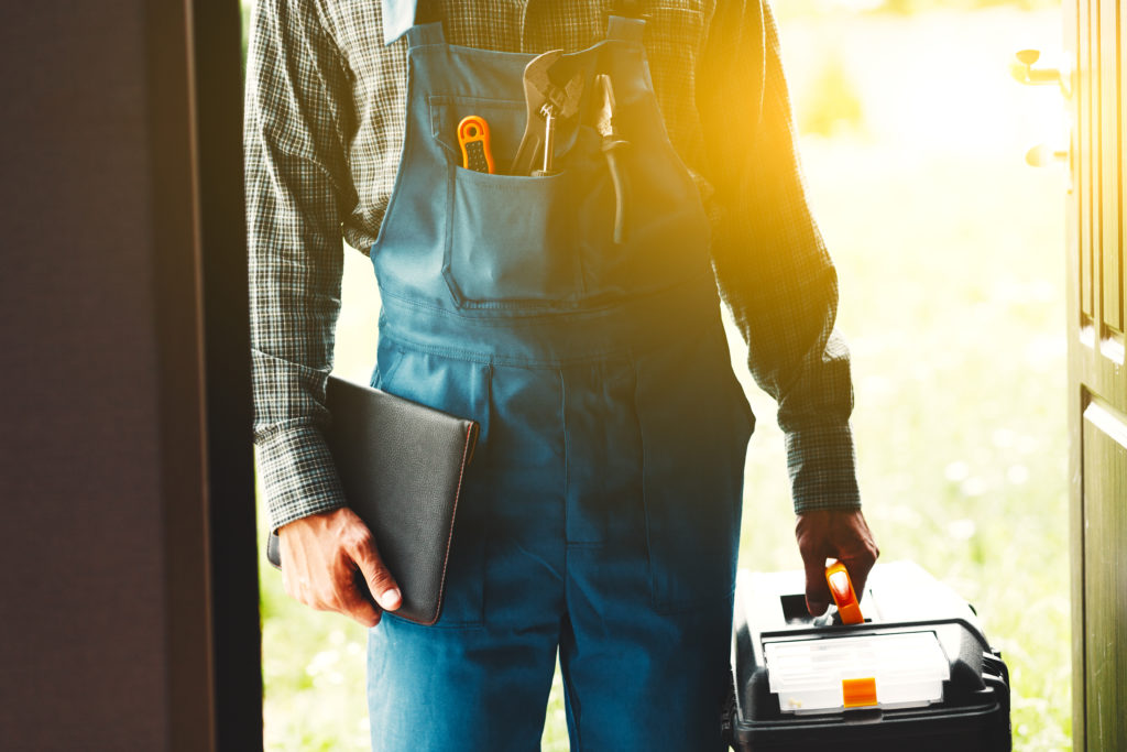 A plumber in a doorway with a case of tools and a notepad.